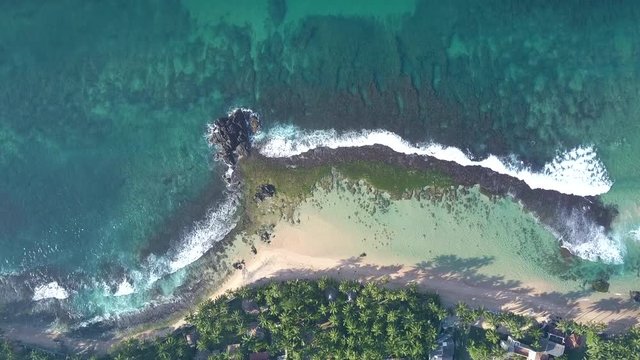 long foamy ocean waves roll on sandy coastline with green grass at palms hiding houses roofs vertical aerial zoom in. Concept best place to live nature