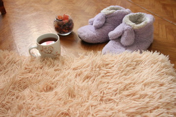 a pair of slippers on the floor next to a mug of tea and a fluffy plaid