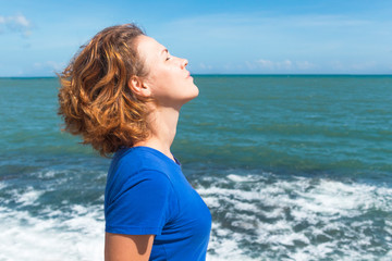 Profile, side view portrait of relaxed woman breathing deeply fresh air on a sea, beach, ocean. Young ginger red hair girl relaxing, sunbathing in the sun with her eyes closed, meditating outdoors.