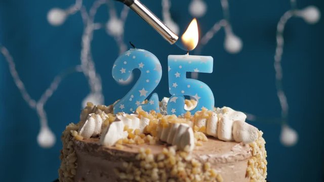 Birthday cake with 25 number candle on blue backgraund. Candles are set on fire. Slow motion and close-up view