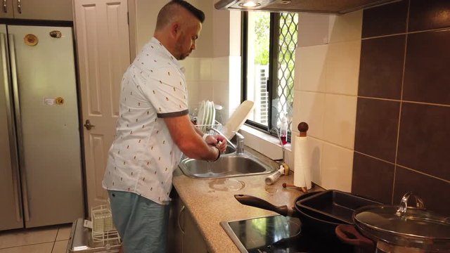 man in the kitchen washing and rinsing a stainless steel milk frothing jug used to make forth for coffees, rinsing and placing the jug in the dish drying rack