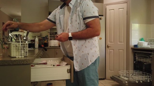 man putting the knives and forks and spoons back in the cutlery draw after putting it through the dishwasher, dishwasher open in the background
