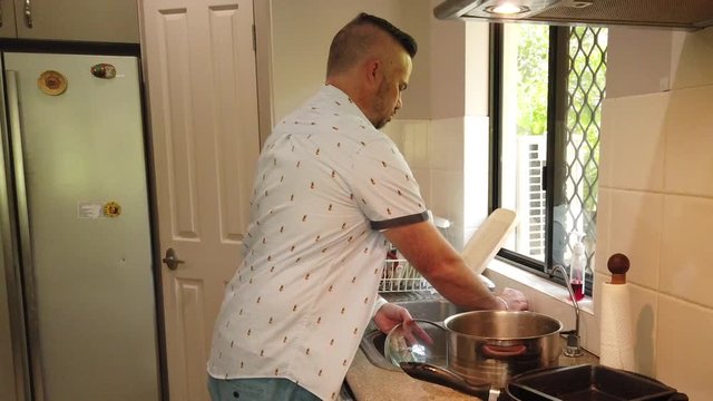 guy scrubbing a cooking pot lid in the sink, rinsing the cooking pot llid and placing the cooking pot lid in the drying rack,
