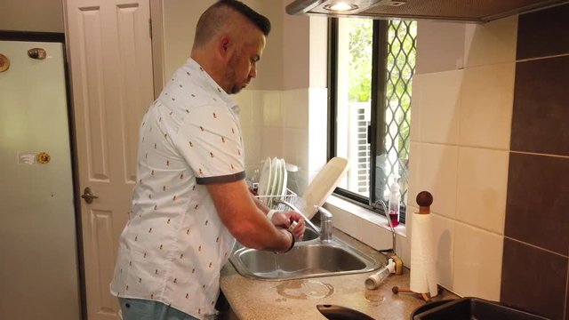 man in the kitchen cleaning the dishes in the sink, cleaning a stainless steel milk jug,