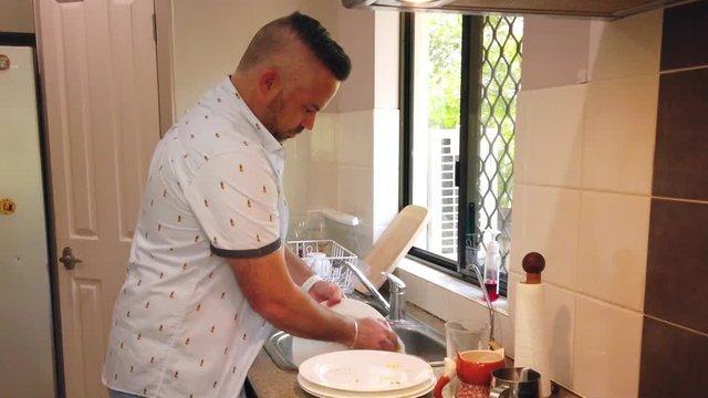 close shot of man washing white plates in the sink, rinsing off the bubble and putting the plates in the dish rack,