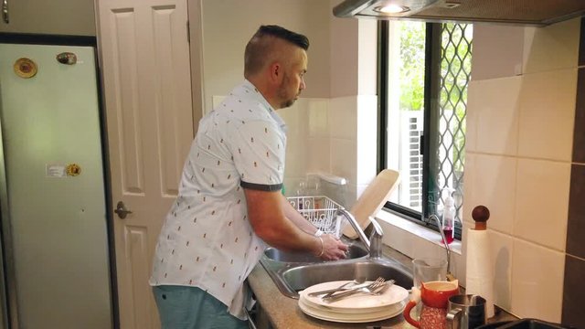 man at the kitchen sink preparing to start washing dishes by filling the sink and adding detergent. Dirty dishes in the shot ready to wash