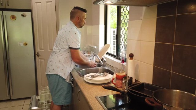 man at the kitchen sink in front of a bright window, filling the sink in preparation for washing the dishes. filling the sink,