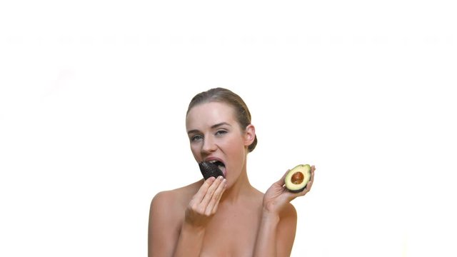Slim, beautiful blond hair model in studio on white background eats fresh avocado. The concept of a healthy lifestyle, vegetarianism and veganism.