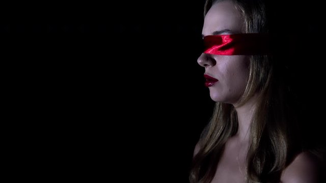 Young woman blindfold with red ribbon over black background. Concept of sexual fetish.