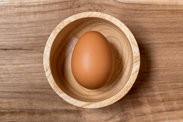 Close up of organic raw egg in wooden bowl isolated on wooden table background.