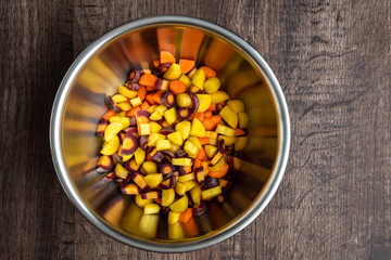 Diced rainbow carrots in a stainless-steel bowl, on a wood table