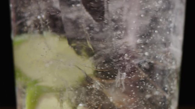 Filling glass of ice and slices of lime with sparkling water macro shot, making a mojito, bubbles in liquid, slow motion, shot on Red Weapon Helium 8k