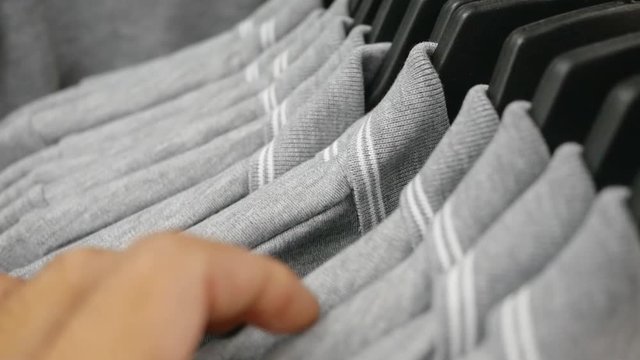 Close up of Man's hands run across a rack of clothes and chooses the shirt.
