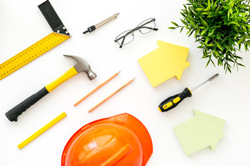 Construction concept. Helmet, tools on work desk, house cutout on white wooden background top-down pattern