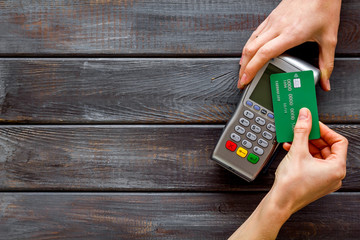 Contactless payment, paypass. Hand hold bank card near terminal on dark wooden background top-down...