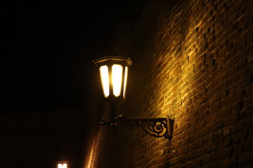  Two street lamps on the brick wall shining in the dark
