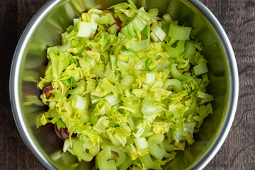 Chopped celery in a stainless-steel bowl, on a wood table