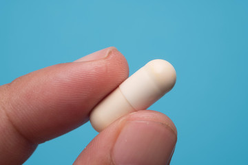 Holding white tablet on blue background, macro shot. Health concept.