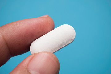 Holding white pill on blue background, macro shot. Health concept.