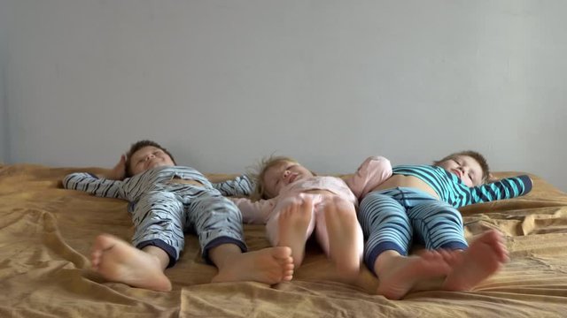 Three happy boys are lying on bed with an elastic mattress. Children talk and move bare feet. Children are happy together during. Christmas holidays. Exercises for preschoolers.