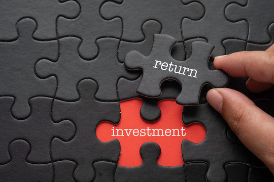 Hand hold piece of puzzle written RETURN revealing word INVESTMENT. Business concept.