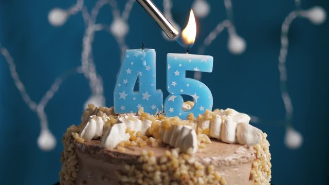 Birthday cake with 45 number candle on blue backgraund. Candles are set on fire. Slow motion and close-up view