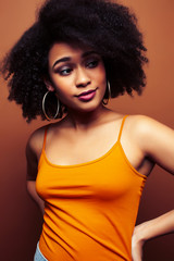 pretty young african american woman with curly hair posing cheerful gesturing on brown background, lifestyle people concept