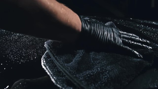 Using rag in palm of your hand, drops are removed from the car. Drop flow down the hood. Close up view of bonnet car. Process of polishing and washing auto. Hose is poured over cowl with water.