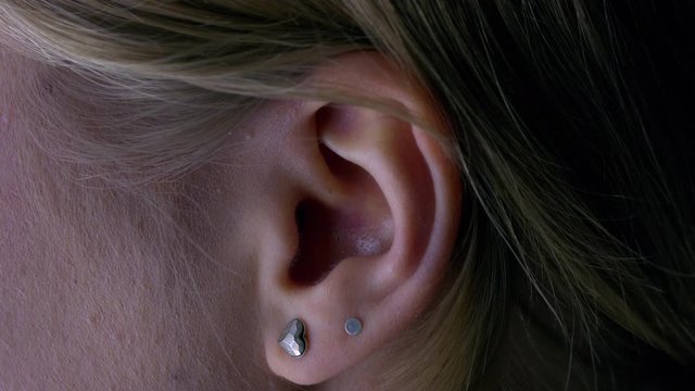 Close-up macro of the ear of a young woman with two earrings. Hearing and ear care concept.