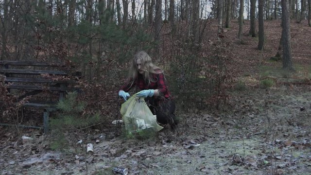 Cleaning environment of plastic trush lying in the forest. Young volunteer woman is picking trash from polluted park.  Protecting and carrying planet Earth from ecological disaster.