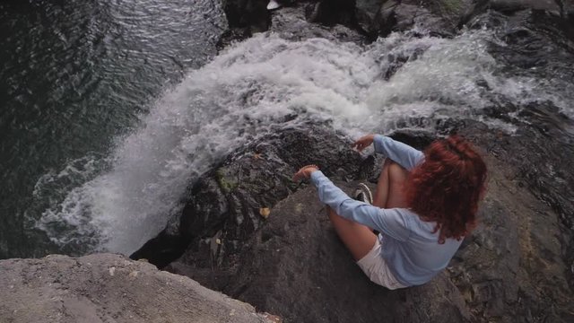 Red-hair curly woman sit on edge near Aling-Aling rushing waterfall