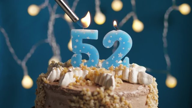 Birthday cake with 52 number candle on blue backgraund. Candles are set on fire. Slow motion and close-up view