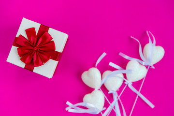 Obraz na płótnie Canvas Festive gift boxes, white decorative hearts on sticks on pink background. Decor for Valentine's Day celebration