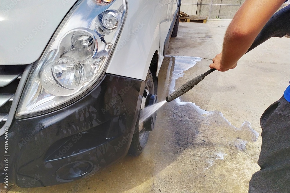 Wall mural high pressure water jet cleaning. a male car wash's worker washing a white minibus using power spray