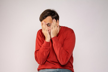 A young man in a red sweater covers his face with his hands