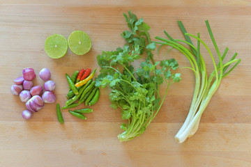 Onions, lemons, coriander, chilli, spring onions on top wood cutting board.