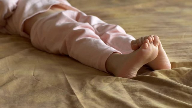 Legs, feet and fingers of boy close-up. Cute blond child in pink pajamas plays with touch screen of smartphone while lying on sofa. the kid wants learn everything. Home teaching for lagging children
