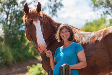 Happy smiling pregnant woman standing with her horse after walking by the river