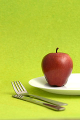 Delicious apple in plate with knife and fork on green background