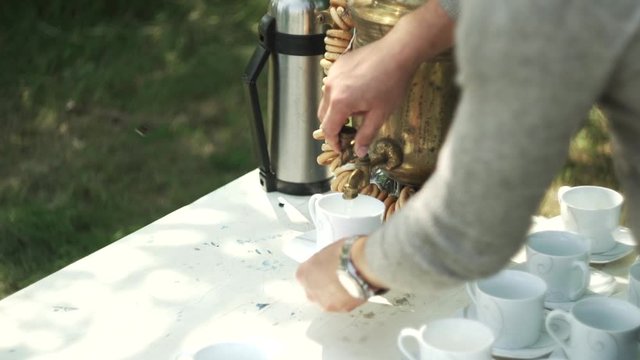 Woman pours boiling water from the samovar into a cup