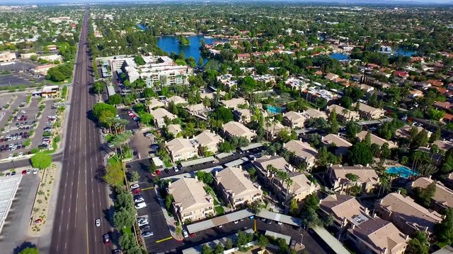 Aerial drone photography over homes on a small lake pulling backwards with traffic. High flying drone shot above a the big city on a sunny day