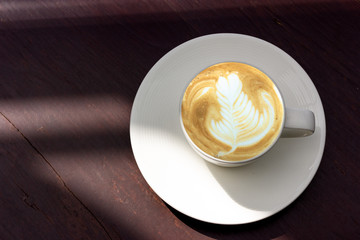 White cup of latte art coffee with shaped rosetta art on brown 