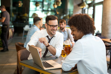 Two businessmen working on the go on a laptop together in a cafe.