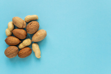 Different nuts on a blue background with copying space. Peanuts, pecans and walnuts in shells