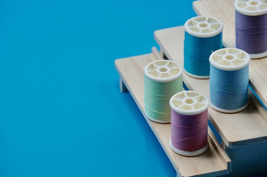 A group of pink, purple, blue, and green thread on the wooden stand on the blue background