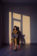 Fototapeta premium Asian woman sitting with laptop looking to camera on wall with light and shadow background.