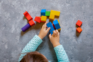 little smiling child playing with colored wooden constructor toy. baby hands close-up playing intellectual toys.  