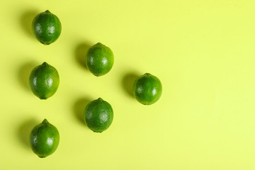 Flat lay composition with fresh juicy limes on yellow background, space for text