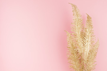 Modern stylish golden festive background - golden glittering palm branch on soft light pastel pink background, top view, copy space.