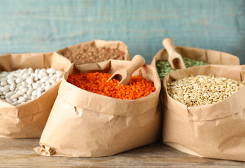 Different grains and cereals in paper bags on wooden table
